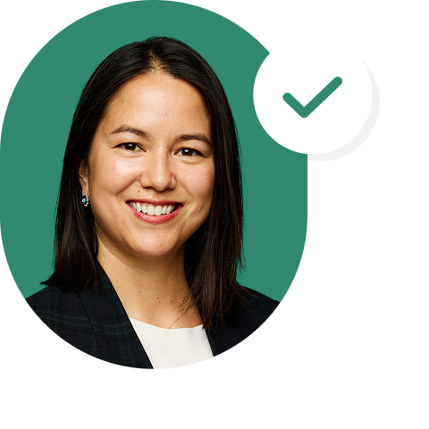 A woman with straight dark hair smiles at the camera. She is wearing a dark blazer and white top. A green checkmark in a white circle appears beside her. The background is green.